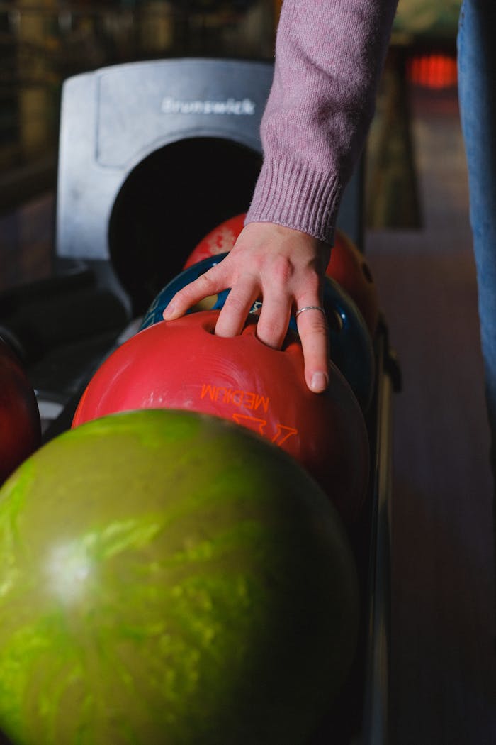 Close-up of a hand choosing a bowling ball at a bowling alley, capturing a weekend leisure activity.